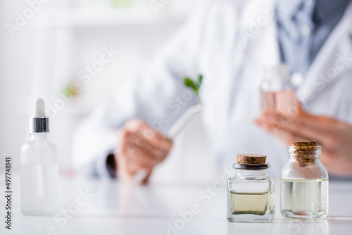 bottles with essential oils near serum and blurred chemist in lab.