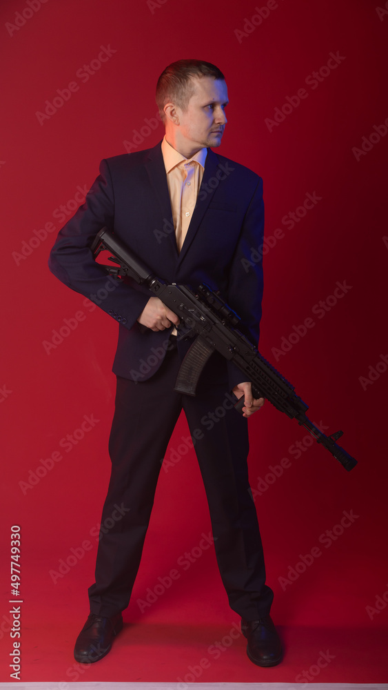 businessman with a gun. a guy in fashionable glasses, a suit holds a machine gun. Business concept. red background businessman with a gun. a guy in fashionable glasses, a suit holds a machine gun. Business concept. red background