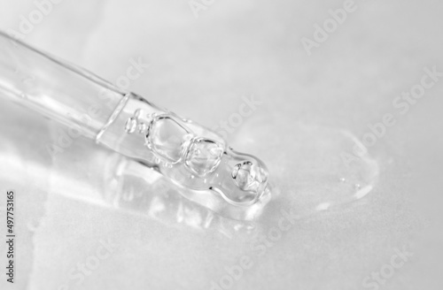 Pipette with fluid hyaluronic acid on gray background. Cosmetics and healthcare concept closeup. Dose of serum, retinol with air bubbles. Flat lay. Luxury beauty product presentation, macro