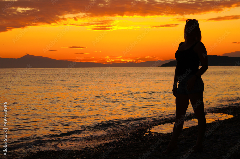 Sunset. Silhouette of a woman on the shore of the Aegean Sea. Greece.
