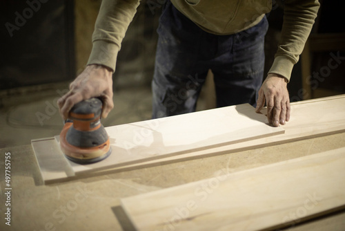 Carpenter grinds wood. Grinding tool. Guy in workshop handles board.