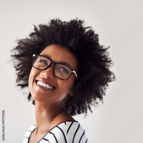 As happy and carefree as can be. Studio shot of an attractive and happy young woman wearing glasses against a gray background.