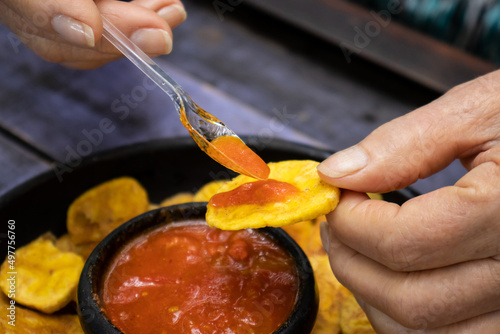 Closeup of woman's hands while eating plantain chips served with Colombian traditional hogao