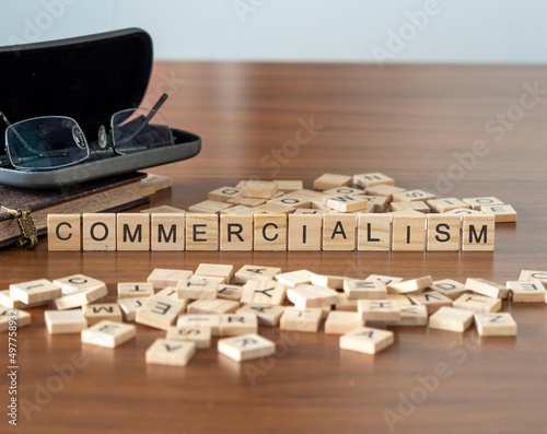 commercialism word or concept represented by wooden letter tiles on a wooden table with glasses and a book