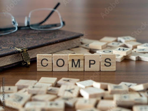 the acronym comps for comparable company analysis word or concept represented by wooden letter tiles on a wooden table with glasses and a book photo