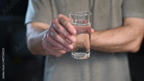 Tremor of the hands when trying to drink. Water splashes from a glass in the hand of a man with tremors, Parkinson's disease.