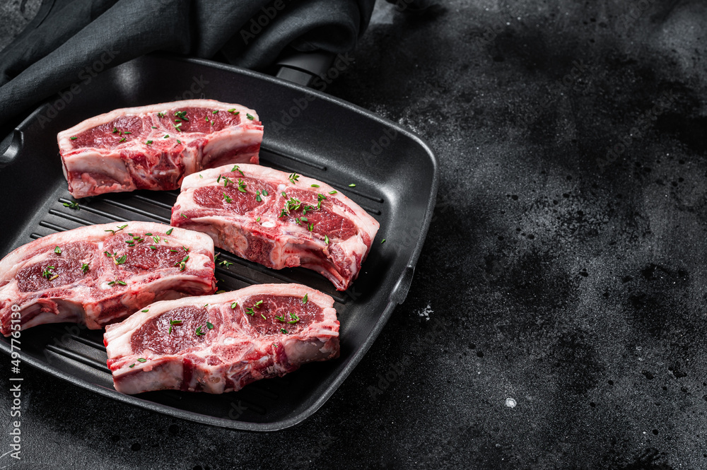 Raw lamb loin rib chops steaks in grill skillet with rosemary and thyme. Black background. Top view. Copy space