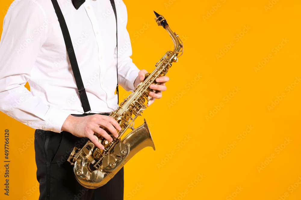 Obraz premium Man in elegant outfit with saxophone on yellow background, closeup. Space for text