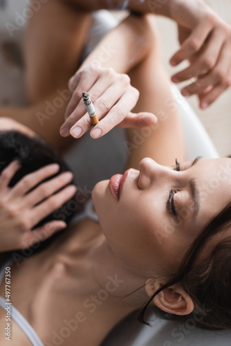 Top view of pretty young woman holding cigarette near blurred man in bathtub.