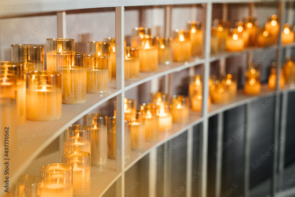 A lot of electric candles in glass cups stand on the shelves and decorate the wedding ceremony. Soft blur and focus. Warm calm design.