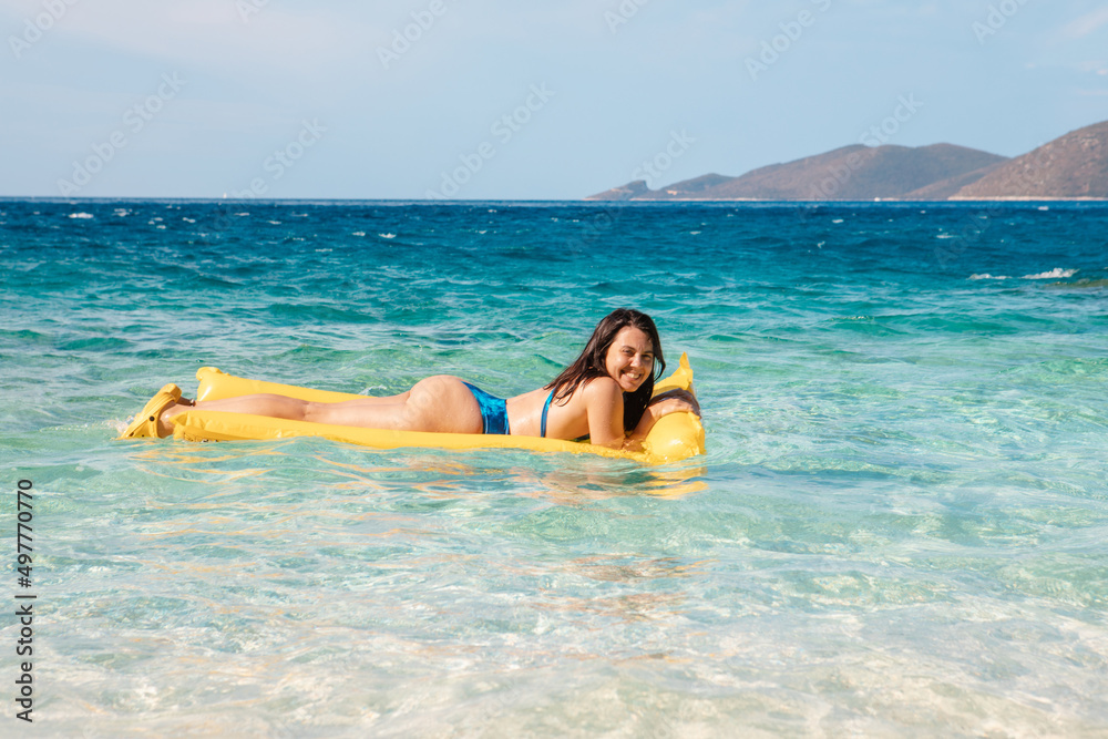 happy woman in blue swimsuit floating on yellow inflatable mattress happy woman in blue swimsuit floating on yellow inflatable mattress