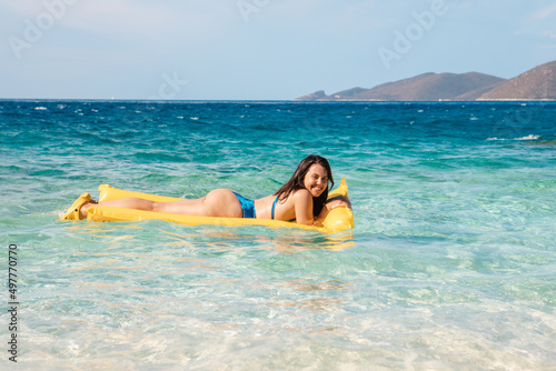 happy woman in blue swimsuit floating on yellow inflatable mattress