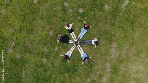 Friends are sitting on the grass with their legs joined in a circle.