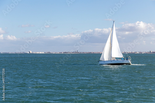 White Yacht sailing in Tagus river with Lisbon cityscape on the background, Portugal