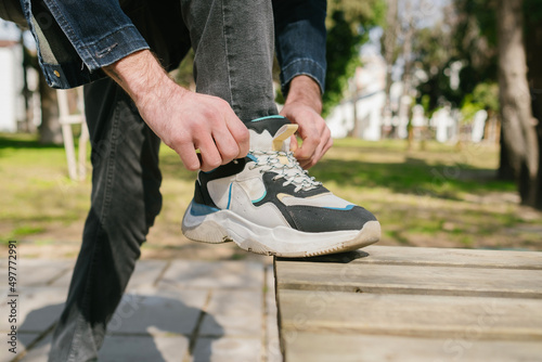 Sport shoes, young man put his foot on park bench and tying shoelaces, a product suitable for daily use with gray and blue details