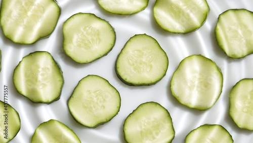 Close-up of single water drop making rings on water surface over cucumber slices arranged in rows on white background | Background for face care product