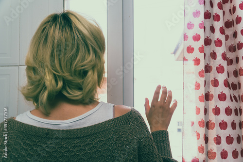 Mujer asomada a la ventana, mujer pensativa mirando por la ventana de la cocina,  photo