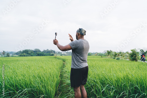 Side view of young male shooting influence content via waterproof modern camera exploring rice fields in Indonesia, millennial hipster guy creating video via digital technology talking about Bali