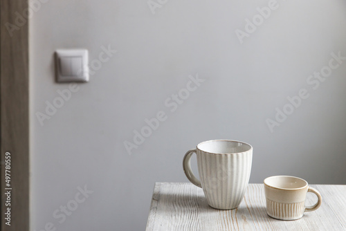 Two porcelain white cups are on the beige table. Large and small cup