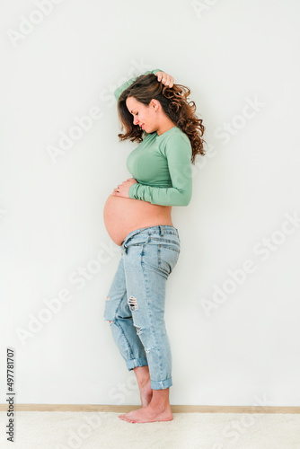 Beautiful young pregnant brunette woman in modern clothes with white background. The concept of motherhood and pregnancy
