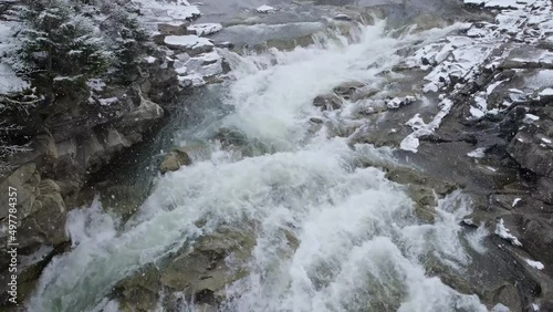 Snowfall above waterfall Probiy on river Prut in Ukrainian Carpathians. Located in the heart of the famous resort Yaremche, Ukraine. Wild Mountain River Flowing with Stone Boulders and Stone Rapids.