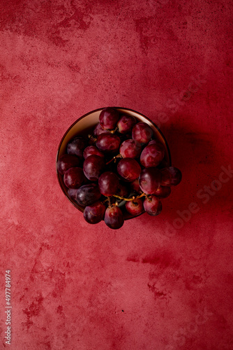 still life raw plums, pomegranate and grapes in a red stone background