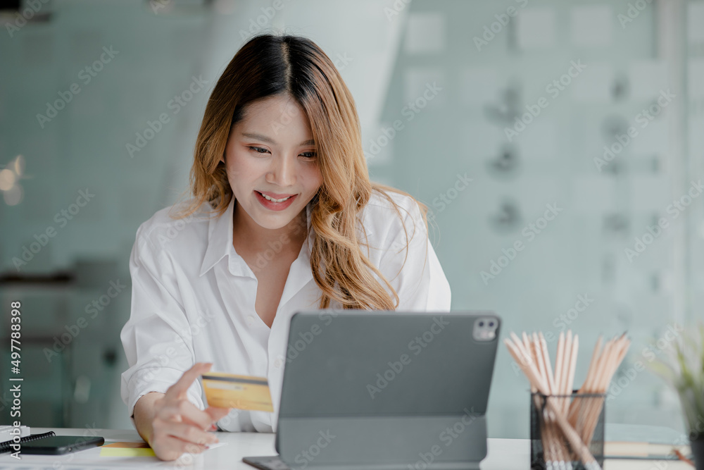 Beautiful woman holding a credit card, she uses a credit card to pay for goods and services online, the concept of using a credit card for online shopping, ordering goods and services on the website. Beautiful woman holding a credit card, she uses a credit card to pay for goods and services online, the concept of using a credit card for online shopping, ordering goods and services on the website.