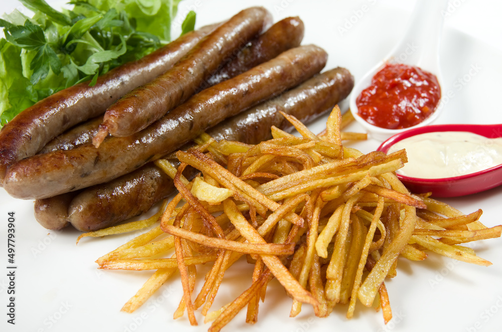 Thin thin hunting sausages with french fries, herbs and sauce on a white dish. Thin thin hunting sausages with french fries, herbs and sauce on a white dish.