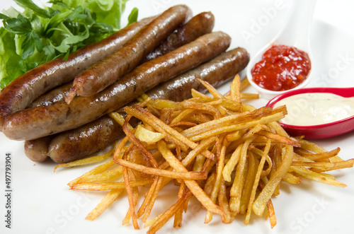 Thin thin hunting sausages with french fries, herbs and sauce on a white dish.
