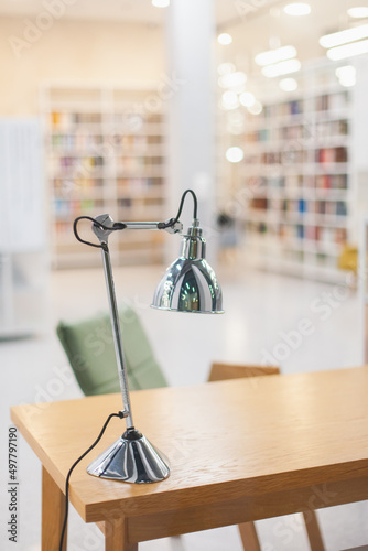 office interior with a metal desk lamp on a wooden desk and bookshelves in bokeh, modern office or university college library interior