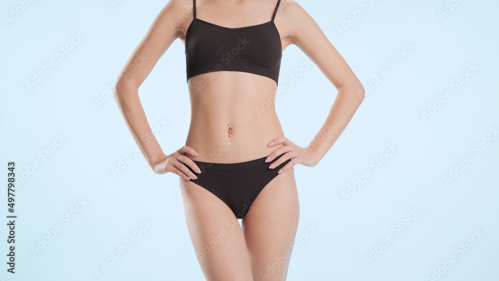 Woman's body. Medium shot of young slim woman in black underwear and hands on her hips on pale blue background | Body care commercial concept