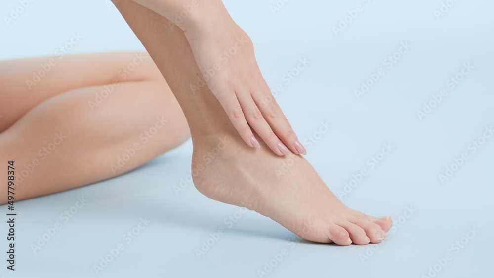 Close-up shot of smooth woman's foot being touched by her hand sitting on the floor on pale blue background | Leg care commercial concept Close-up shot of smooth woman's foot being touched by her hand sitting on the floor on pale blue background | Leg care commercial concept