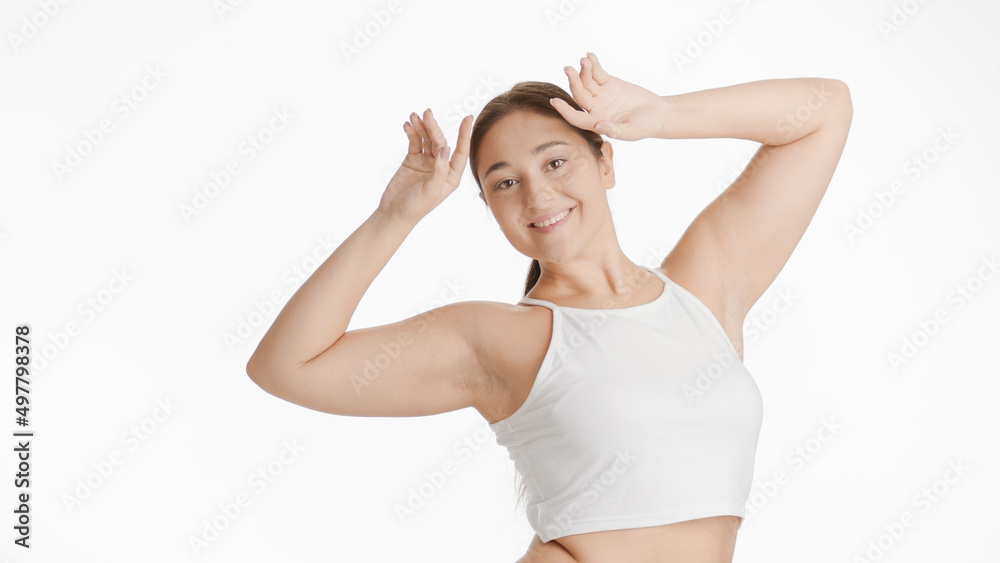 Young dark-haired Caucasian plus size woman in white top raises her hands up to her head smiling wide for the camera on white background | Depilation concept Young dark-haired Caucasian plus size woman in white top raises her hands up to her head smiling wide for the camera on white background | Depilation concept