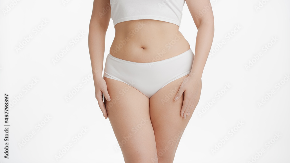 Horizontal medium shot of white-skinned plus size woman in white underwear strokes her body on white background | Body care concept