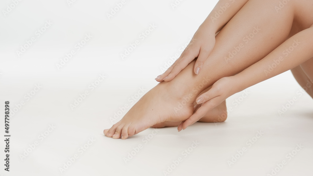 Close-up shot of white-skinned woman touches her smooth feet sitting on white background | Anti cracked foot concept