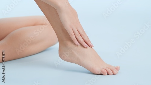 Close-up shot of smooth woman's foot being touched by her hand sitting on the floor on pale blue background | Leg care commercial concept