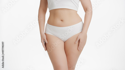 Horizontal medium shot of white-skinned plus size woman in white underwear strokes her body on white background | Body care concept