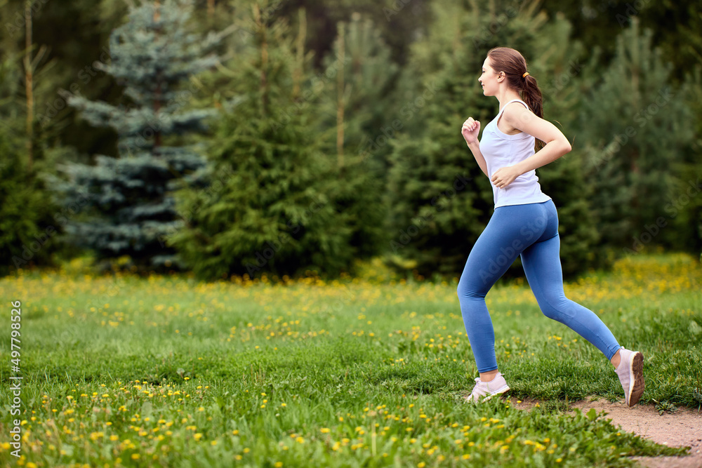 Jogging in public park in summer by active woman in sportswear.