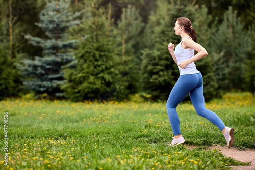Jogging in public park in summer by active woman in sportswear.