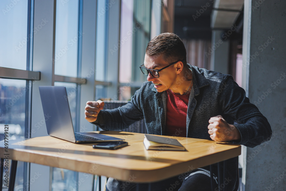 Portrait of a man, IT professional, working remotely with a modern laptop, sitting at a table and smiling at the camera during a break, a happy human programmer in vision correction glasses Portrait of a man, IT professional, working remotely with a modern laptop, sitting at a table and smiling at the camera during a break, a happy human programmer in vision correction glasses