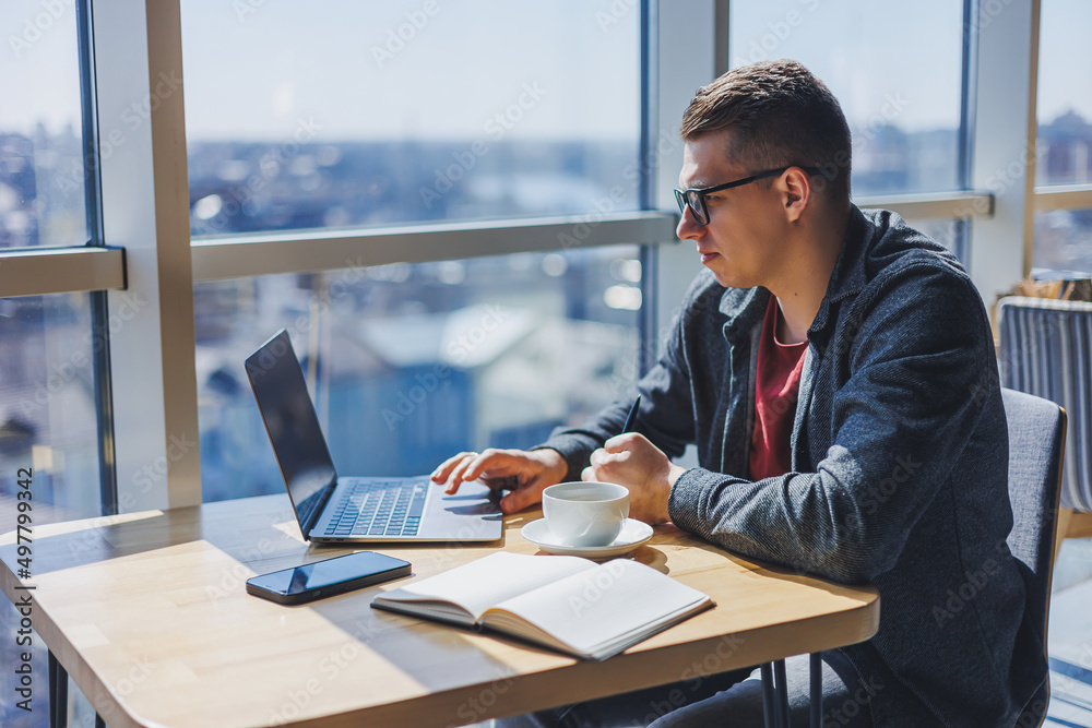Portrait of a man, IT professional, working remotely with a modern laptop, sitting at a table and smiling at the camera during a break, a happy human programmer in vision correction glasses Portrait of a man, IT professional, working remotely with a modern laptop, sitting at a table and smiling at the camera during a break, a happy human programmer in vision correction glasses