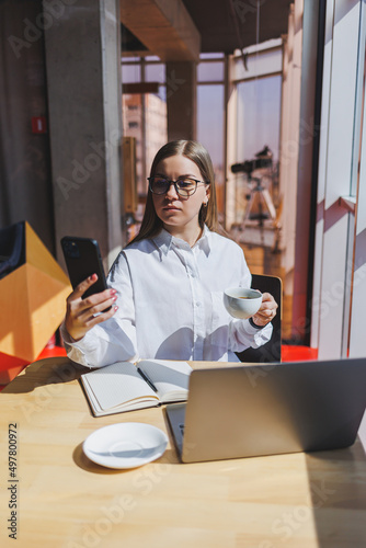 Businesswoman manager in a white shirt doing office work and smiling, successful european female boss in optical glasses for vision correction, posing at a table in a workspace