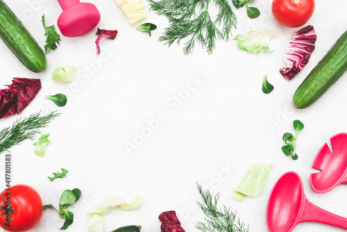 Lettuce leaves, cucumbers, tomato, fresh dill, dumbbell and lettuce spoons on a light cement . photo