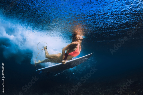 Surfer girl dive with surfboard under wave in transparent Pacific ocean.