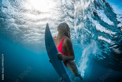 Portrait of surfer girl with surfboard dive underwater with under wave and sunlight in tropical ocean.