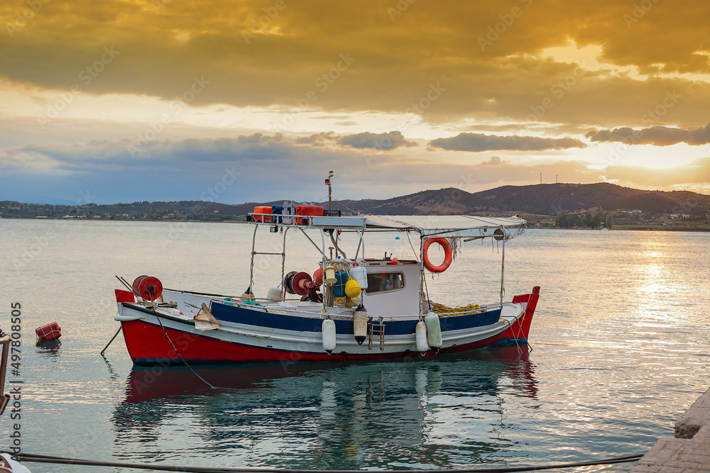 Fishing boat in front of the old wooden pier of greece village at sunset