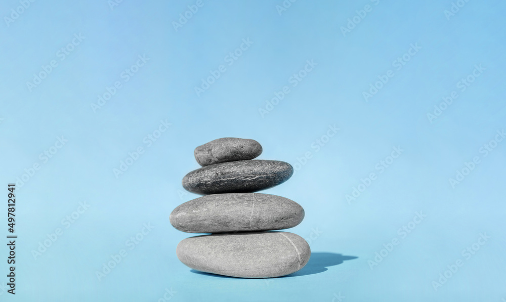 Balanced pebble stones for spa treatments on blue background. The balancing cairn - symbol of harmony, tranquility and relaxation, concept of meditation. Stack of spa hot stones. Balanced pebble stones for spa treatments on blue background. The balancing cairn - symbol of harmony, tranquility and relaxation, concept of meditation. Stack of spa hot stones.
