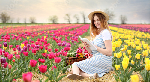 Beautiful young woman reading book in blossoming tulip field on spring day