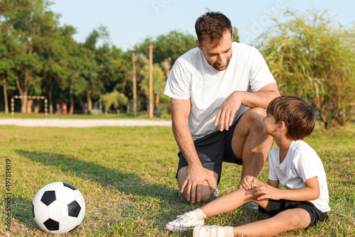 Father and his little son with bruised knee after playing soccer on field