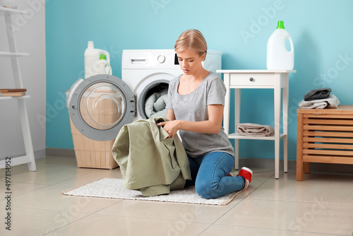 Young woman checking pocket of green jacket before washing in bathroom